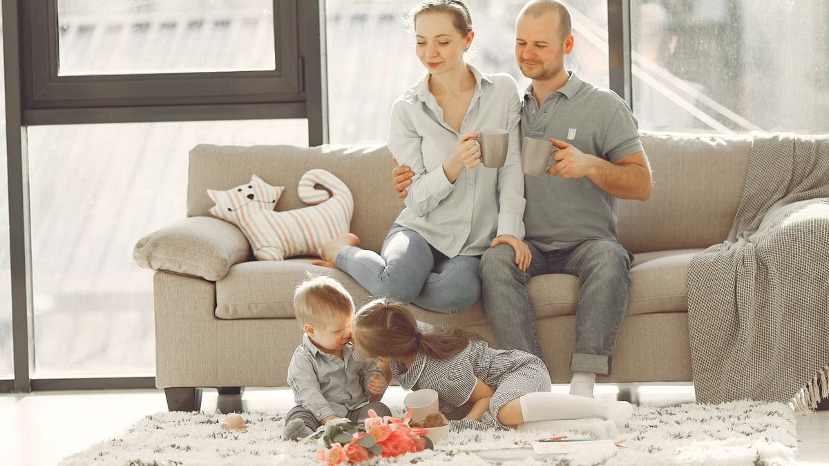 Cheerful family smiling while spending weekend together sitting parents sitting on comfortable sofa while children resting on carpet and playing